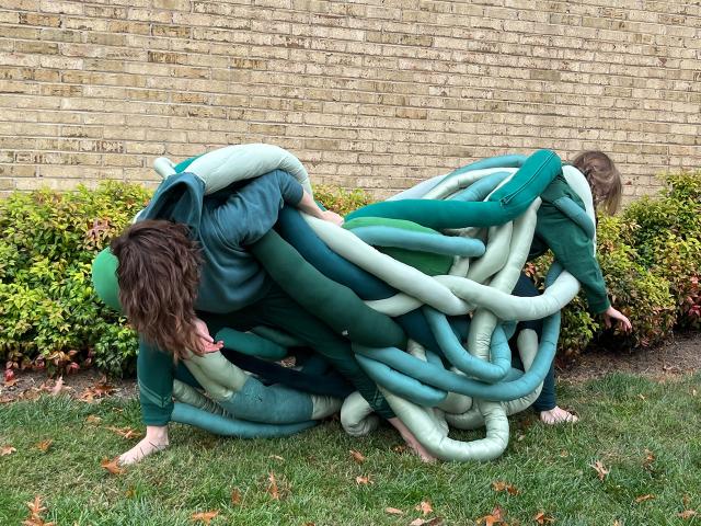 two performers tangles in a green sculpture